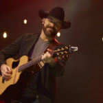 George Canyon playing the guitar on a warmly lit stage at the Algonquin Commons Theatre