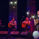 Four singer-songwriters play an acoustic and intimate set on stage at the Algonquin Commons Theatre with Edison lightbulbs behind them