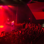 The band Prozzak plays on a red-lit stage at the Algonquin Commons Theatre. You can see the floor and main level audience from the balcony view of the photo